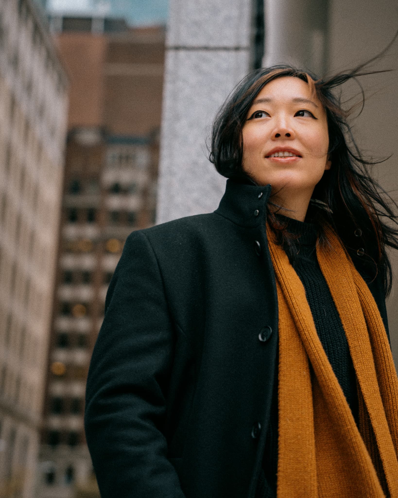 Woman in a black coat and mustard scarf on a city street