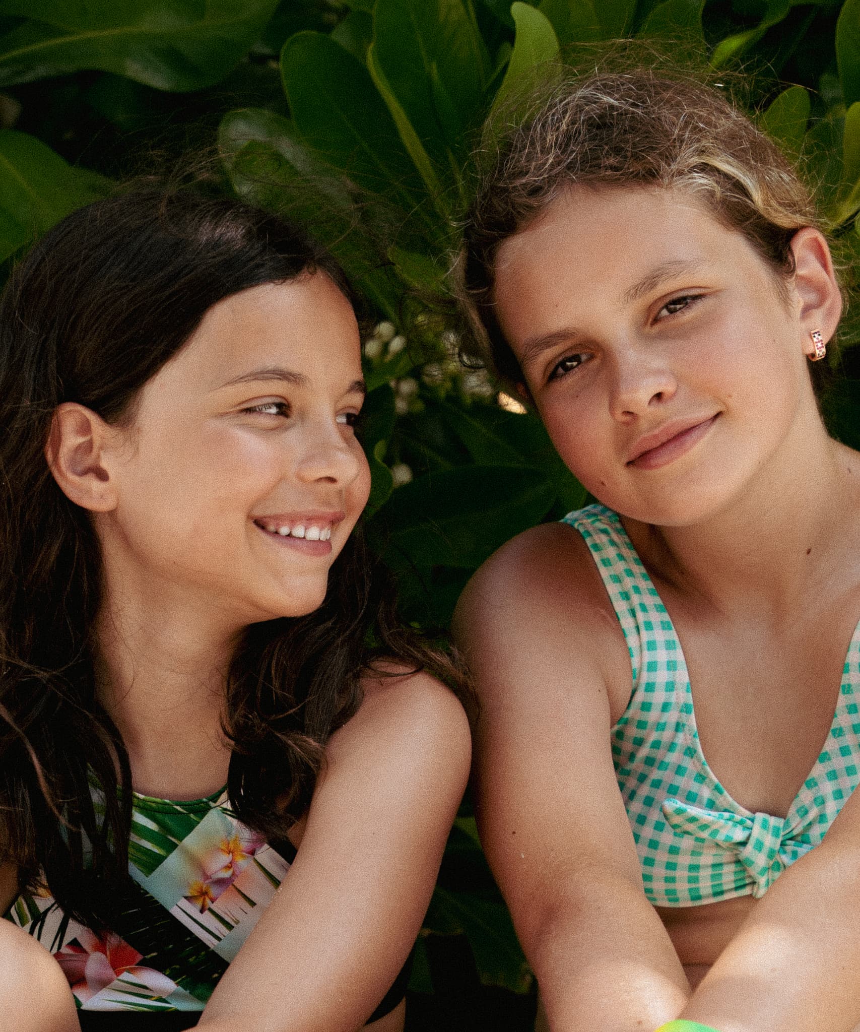 Two girls smiling close together against leafy greenery