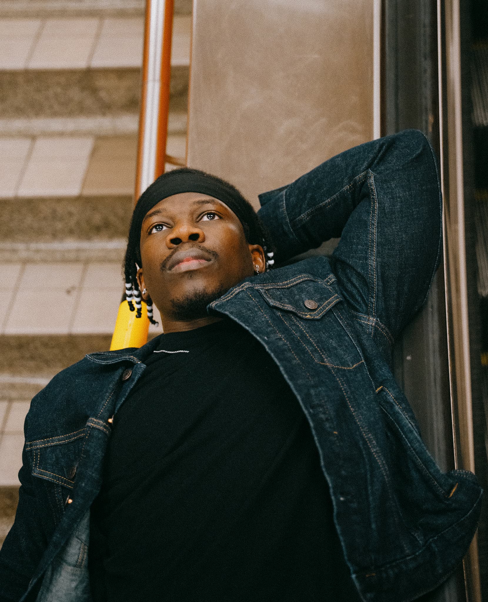 Man reclining on stairs in a denim jacket and beanie